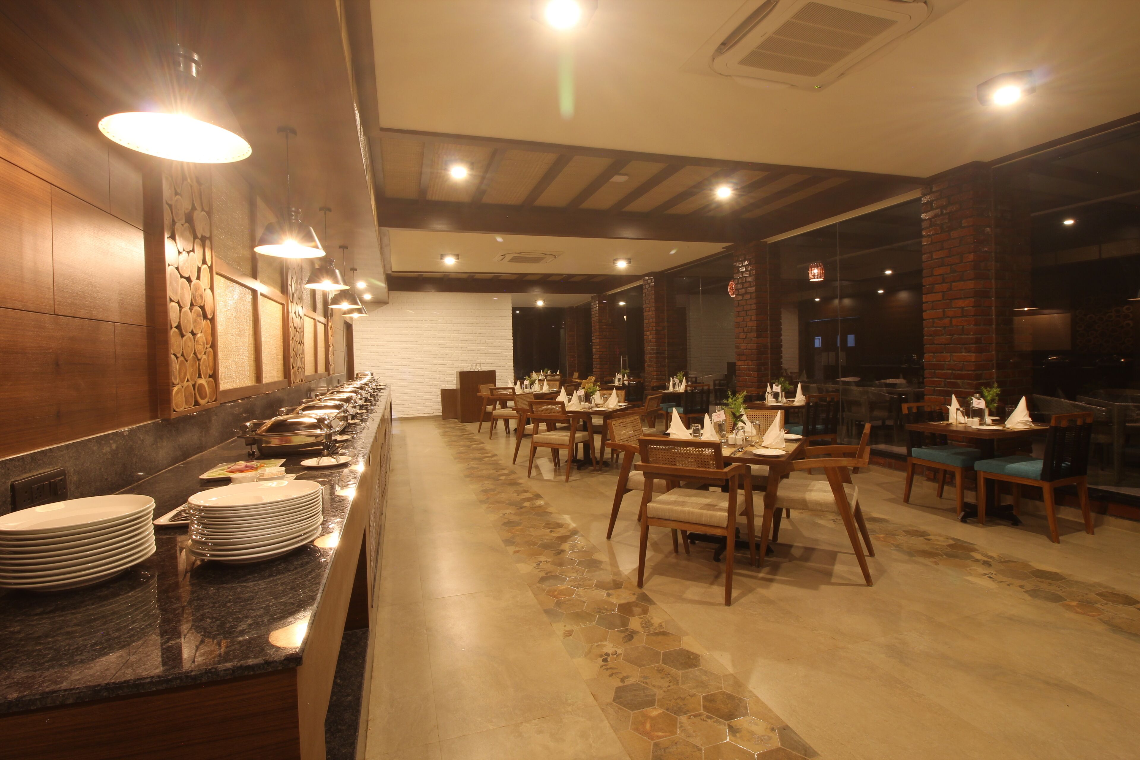 Un restaurante con una larga barra, varias mesas y sillas. Hay platos apilados en la barra y el piso tiene un diseño estampado.
