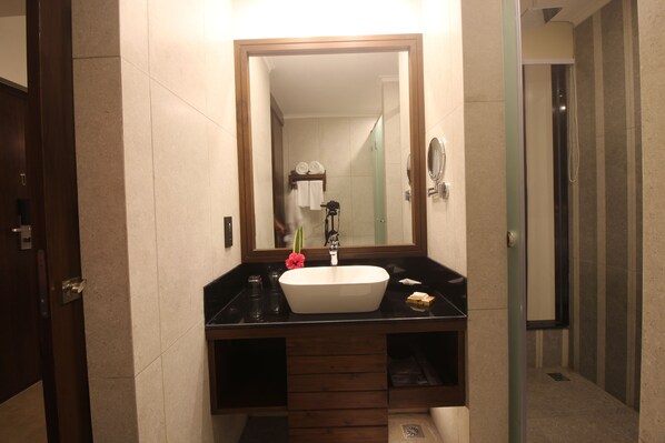 A modern bathroom with a large mirror, a white sink, and a dark countertop. - Regenta Jungle Resort Kabini Springs (Heggadadevankote)