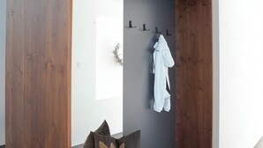 A modern, minimalist room with a wooden bench, a grey wall, and a white robe hanging on a hook. - Vacation apartment for up to 8 people (Latsch/Morter)