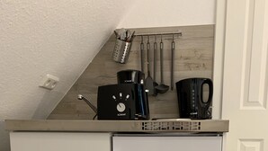 A compact kitchenette with a white refrigerator, a coffee maker, and utensils hanging on the wall. - Bernsteinsucher (Norden)