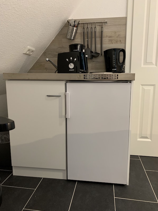A compact kitchenette with a white refrigerator, a coffee maker, and utensils hanging on the wall. - Bernsteinsucher (Norden)
