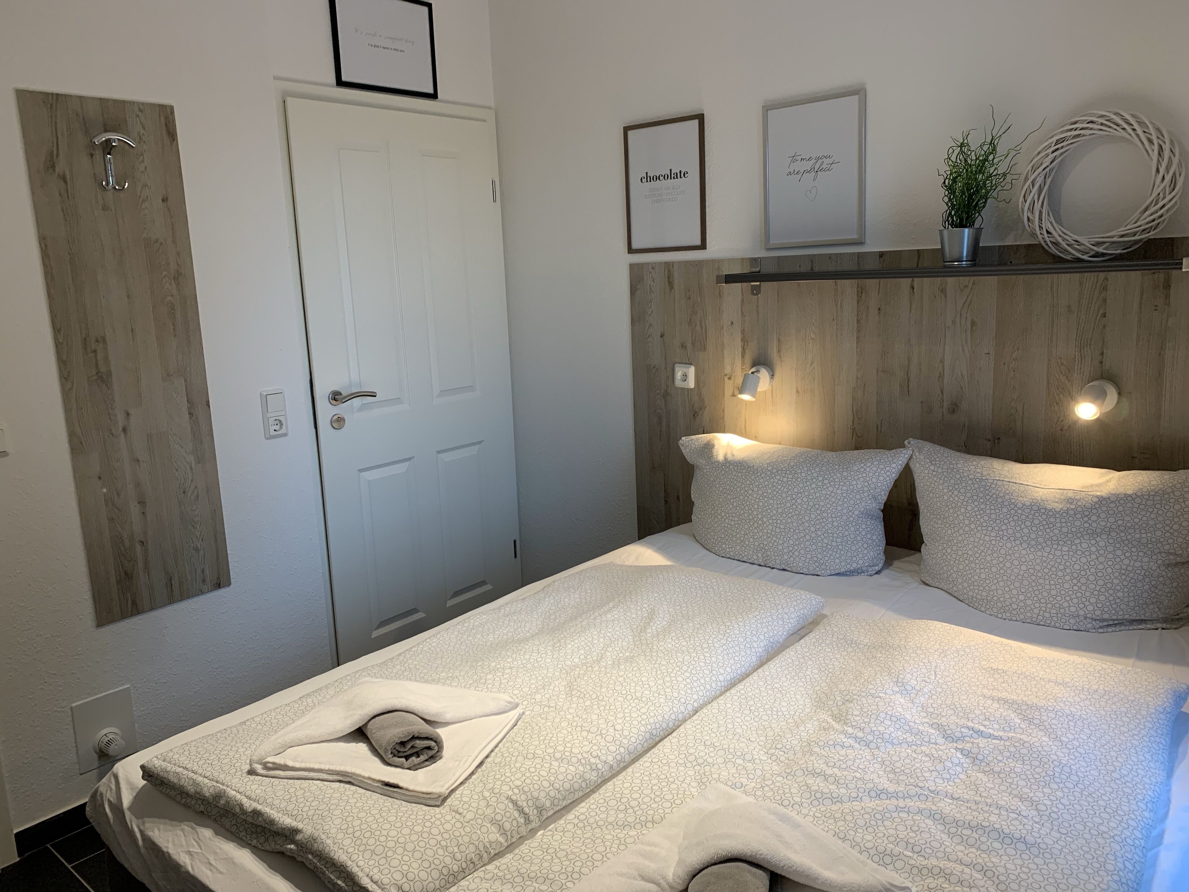 A bedroom with a wooden headboard, a bed with patterned bedding, a white door, and wall-mounted light fixtures.