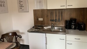A compact kitchen with white cabinets, a stainless steel sink, and a coffee maker. - Bernsteinsucher (Norden)