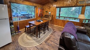 L’intérieur d’un chalet en bois comprend une table à manger, des chaises, un canapé, un réfrigérateur et de grandes fenêtres qui offrent une vue sur l’extérieur.