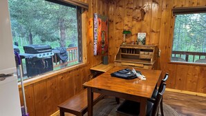 L’intérieur d’un chalet en bois comprend une table à manger, des chaises, un banc, un barbecue à l’extérieur de la fenêtre et une bibliothèque.
