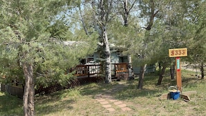 Une cabane dotée d’une terrasse en bois et d’un sentier menant à celle-ci, le tout entouré d’arbres.