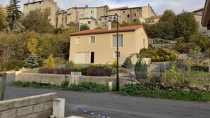 A residential building with a red-tiled roof, a small front yard with a fence, and a street in front. - Villa near village center (Pradelles)