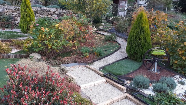 A garden with a winding path, various shrubs, and a decorative wheel. - Villa near village center (Pradelles)
