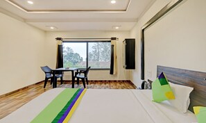 A hotel room with a bed, a table with chairs, a window with curtains, and a television on the wall. - Treebo Paradise Inn, Panchgani (Mahabaleshwar)