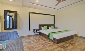 A hotel room with a bed, a nightstand, a mirror, a ceiling fan, and a seating area with a table. - Treebo Paradise Inn, Panchgani (Mahabaleshwar)