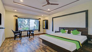 A hotel room with a large bed, a desk with chairs, a ceiling fan, and a view of trees through the window. - Treebo Paradise Inn, Panchgani (Mahabaleshwar)