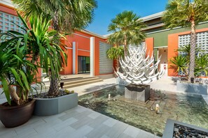 Een binnentuin met een waterpartij, palmbomen en een modern gebouw met een geometrisch gevelontwerp.
