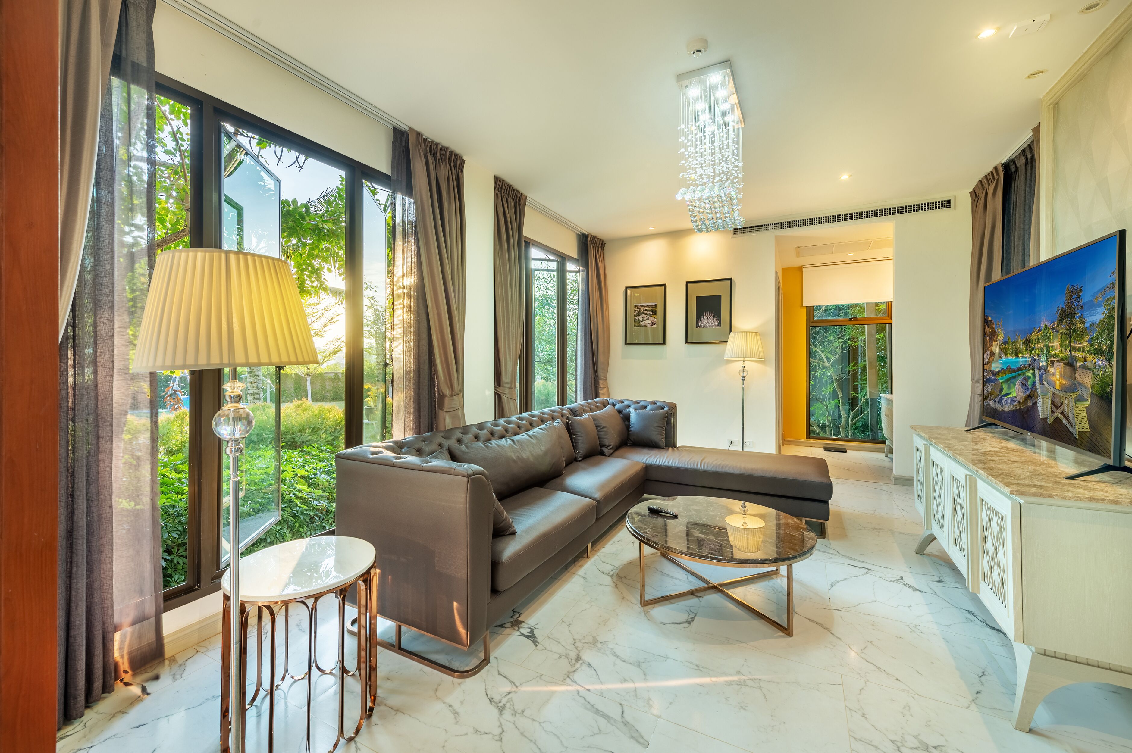 A modern living room with a leather sectional sofa, a glass coffee table, and large windows with curtains.