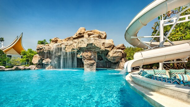 Una piscina con cascada, tobogán de agua y un edificio de estilo tradicional.
