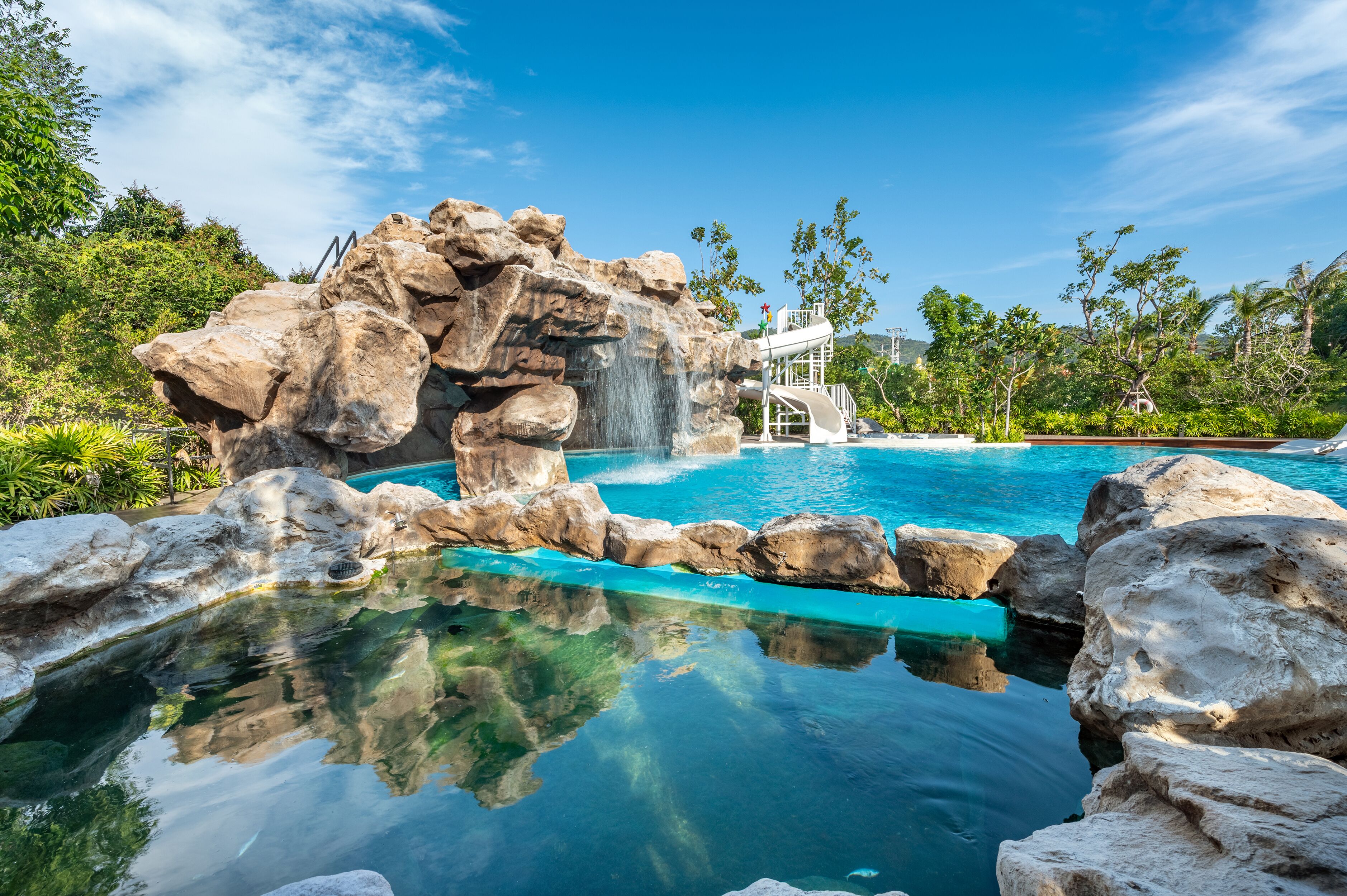 A pool with clear blue water, surrounded by large rocks and greenery.