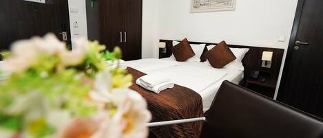 A hotel room with a neatly made bed, a bedside table with a lamp, a nightstand, and a wall-mounted painting.