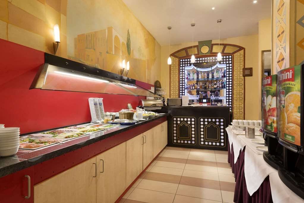Ein Buffetbereich mit einer Theke, die verschiedene Speisen präsentiert, einer Getränkestation und einer Wand mit geometrischem Muster.