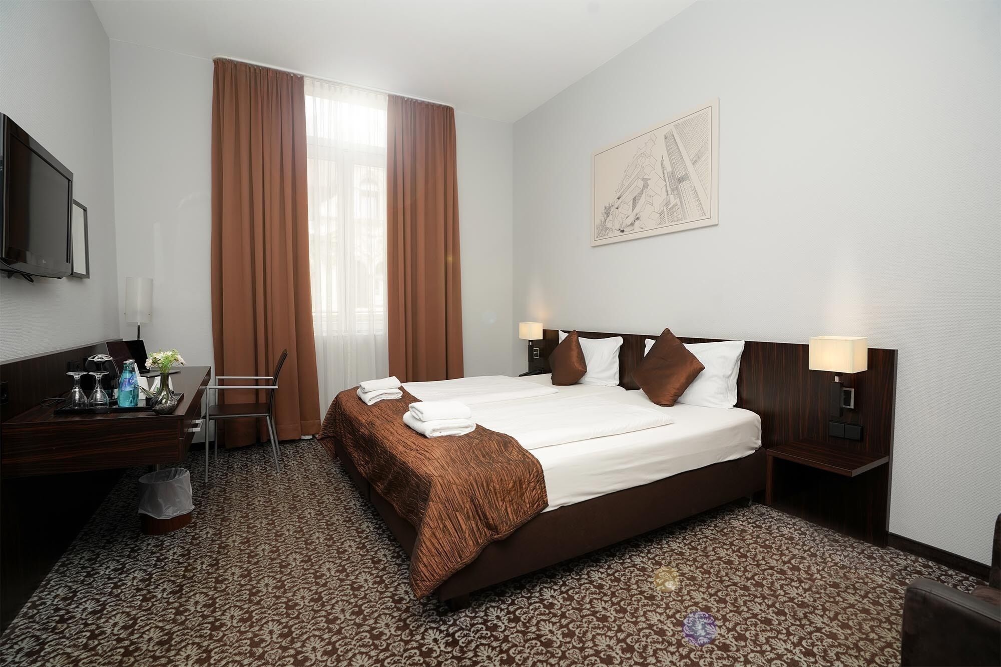 A hotel room with a large bed, a desk with a chair, a TV, and a window with curtains.