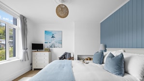 Ein Schlafzimmer mit einem Bett, einem Fernseher, einem Gemälde und einem Fenster mit Vorhängen.