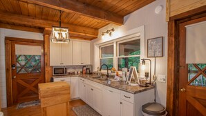 Una cocina con armarios blancos, encimera de granito, pileta de acero inoxidable y techo de madera.