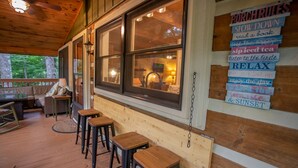 Una terraza de madera acogedora con una zona de bar, taburetes de madera y vistas del interior a través de grandes ventanales.