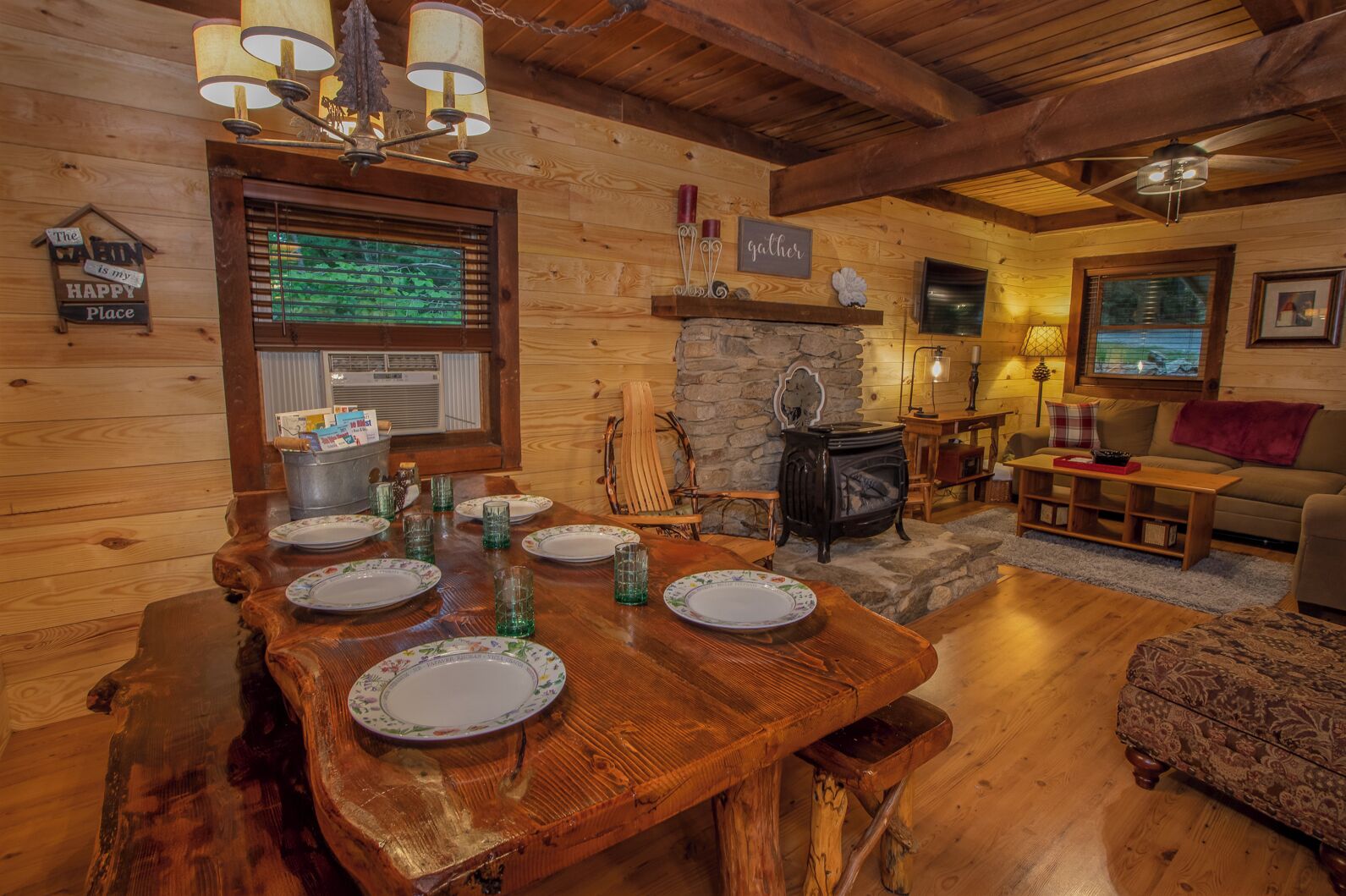 L’intérieur chaleureux d’un chalet avec une table à manger dressée pour quatre personnes, une cheminée, des murs en bois et un coin salon confortable.