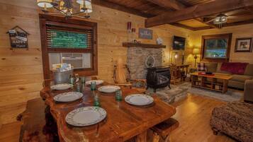L’intérieur chaleureux d’un chalet avec une table à manger dressée pour quatre personnes, une cheminée, des murs en bois et un coin salon confortable.