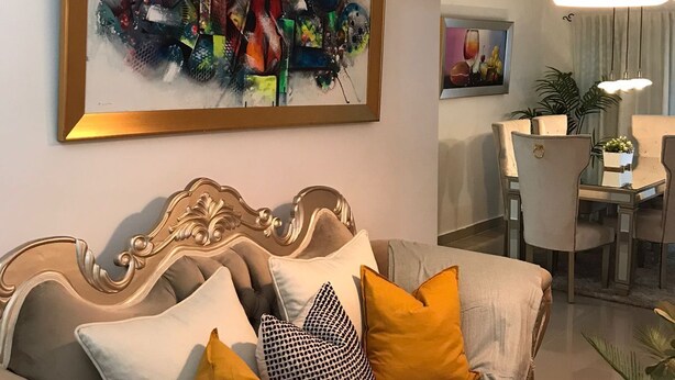 A living room with a sofa, a dining area with a table and chairs, and a large abstract painting on the wall.