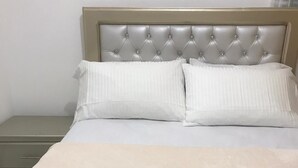 A neatly made bed with a tufted headboard, white bedding, and a beige throw blanket.