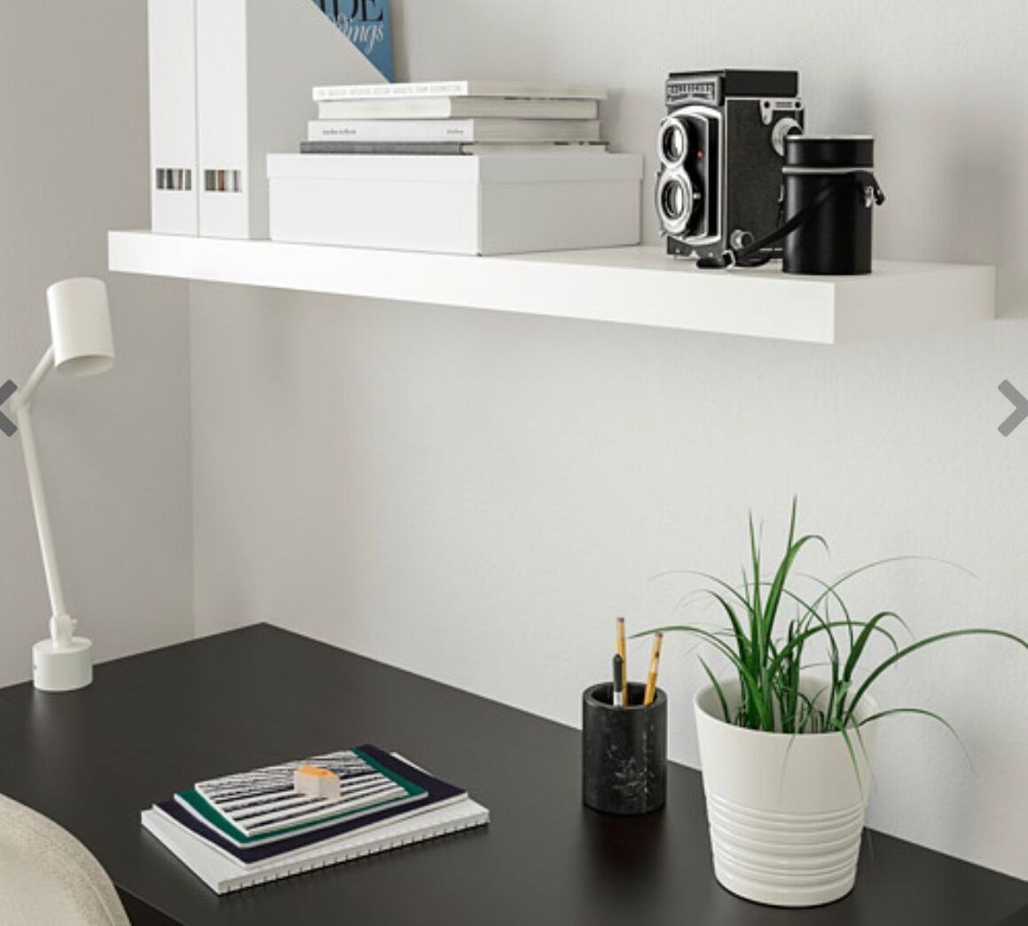 A neatly organized workspace with a white desk, a white lamp, a potted plant, a stack of books, and a vintage camera.