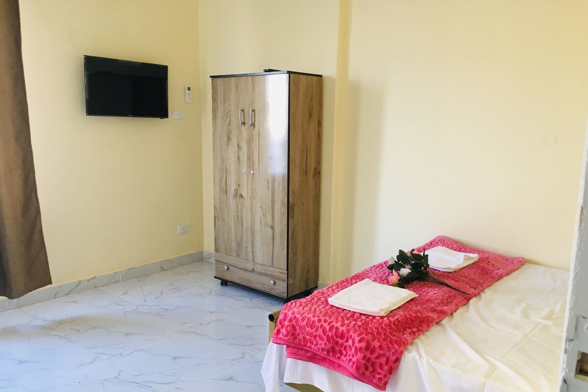 Una stanza con un letto, un armadio e una televisione a schermo piatto appesa al muro.