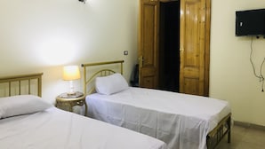 Ein Zimmer mit zwei Einzelbetten, einer Nachttischlampe, einer Holztür und einem an der Wand befestigten Fernseher.