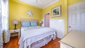 Un dormitorio con cama, dos mesitas de noche, ventilador de techo, decoración con estrellas, una puerta y un aparador.