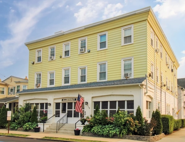 A yellow building with a sign reading "ALLENHURST" and an American flag. - 1BR Apt 2 Blocks to Beach & Main Ave | Full Kitchen | Near Asbury Boardwalk (Ocean Grove)