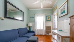Una sala de estar con un sofá azul, un ventilador de techo blanco y una consola blanca.