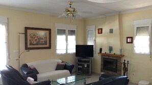 Un salon comprenant un canapé, des fauteuils, une table basse en verre, un téléviseur, une cheminée et un ventilateur de plafond.