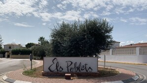 Un panneau indiquant « Els Poblets », placé dans un espace aménagé avec une route pavée et un arbre.