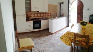 A compact kitchen with white cabinets, a stove, and a dining area with a table and chairs.
