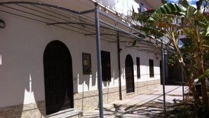 A building with a covered walkway, arched doorways, and a tiled patio area.