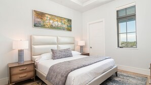 A bedroom with a bed, two bedside tables, a nightstand, a painting, a window, and a door. - SOCE FLATS 305 - Brand New Olde Naples Condo Steps to 5th Ave S! (Naples)