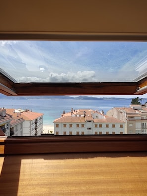 A view from a room with a skylight, overlooking a coastal area with buildings and a beach. - Apartment in Sanxenxo. Penthouse with a view of the sea. (Sanxenxo)