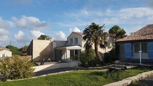 A two-story house with a covered patio, a stone wall, and a palm tree. - Gaia, housse, 4 à 6 P, South Vendée, Puy du Fou, Marais Poitevin (CEZAIS)