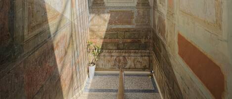 Un corridoio stretto con una finestra a lucernario, pareti decorate e un dipinto centrale.