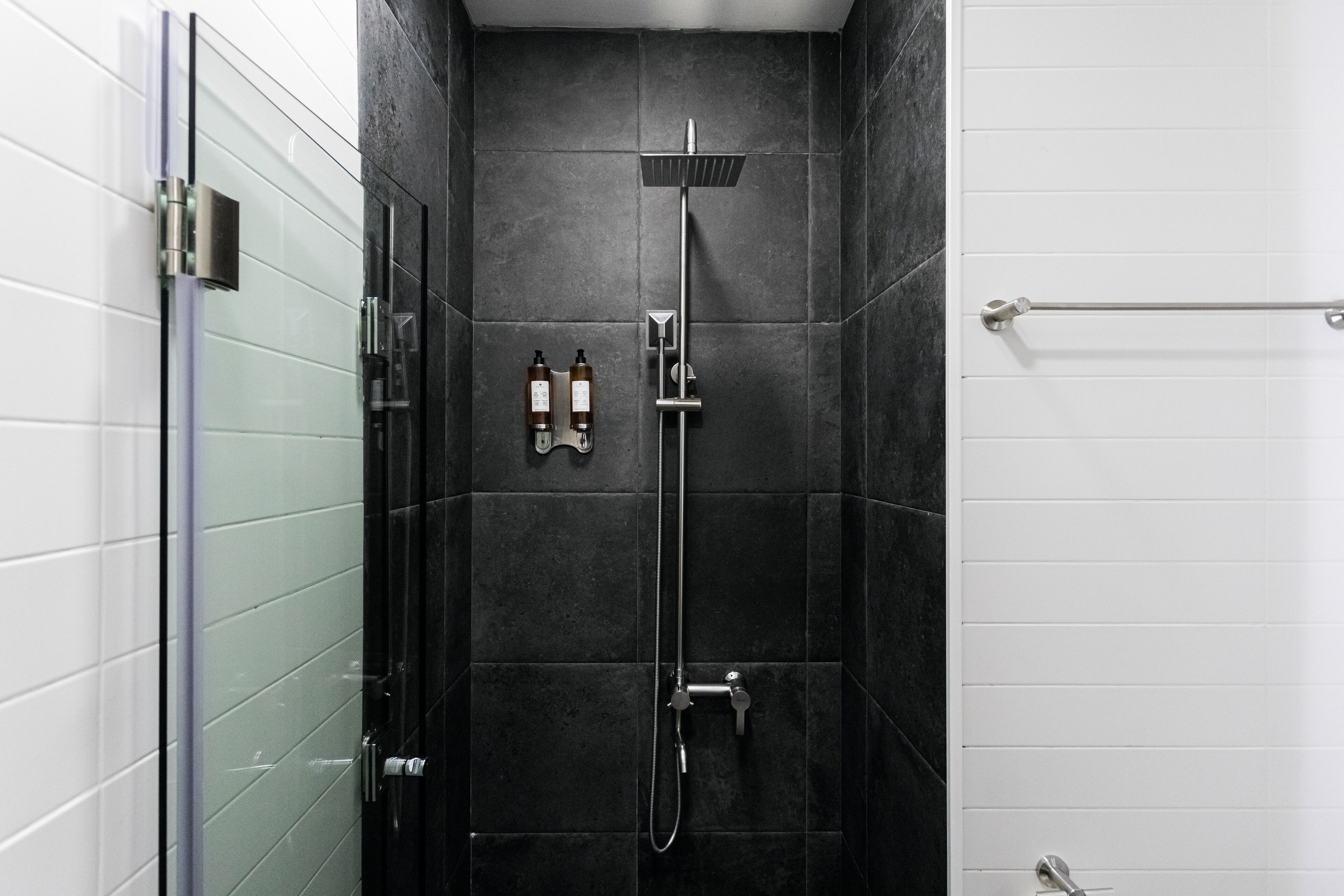A modern shower with a glass door, a handheld showerhead, and two bottles of shampoo and conditioner on the wall.