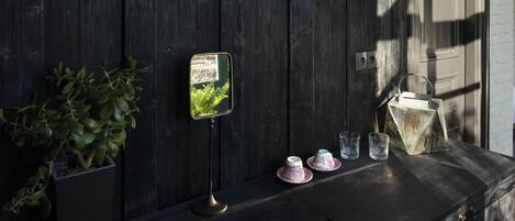 Una pared de madera oscura con un perchero metálico, un cuadro enmarco, una planta en maceta y una pequeña mesa con tazas y un vaso.