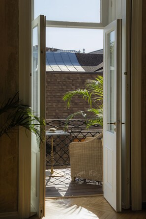 An open door leading to a balcony with a wicker chair, a table, and a potted plant. - Unfound Door (Tbilisi)