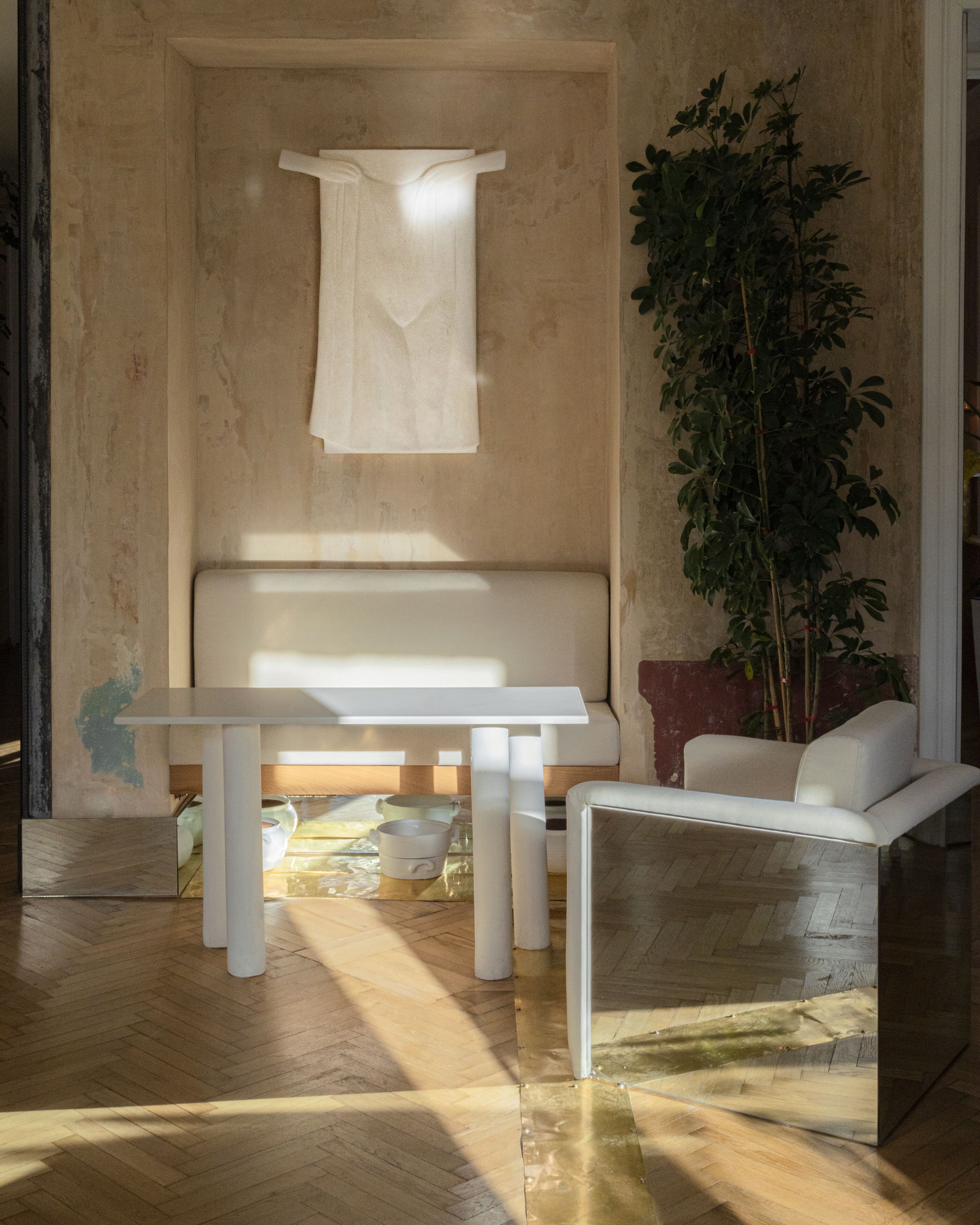 Un interior moderno con piso de madera, un banco blanco, una mesa y una planta grande.