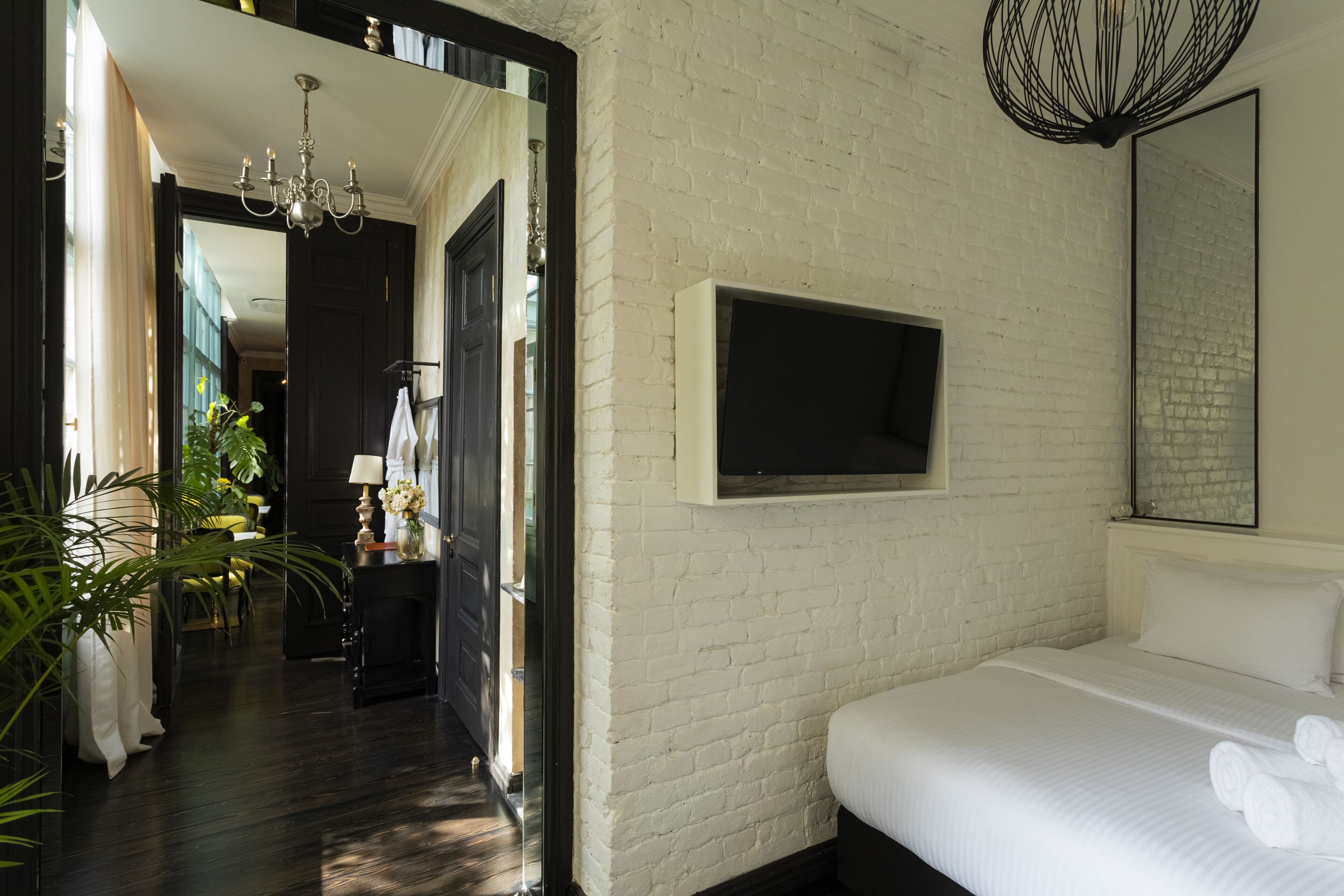 Een hotelkamer met een witte baksteenmuur, een bed met witte lakens, een wandtelevisie en een kroonluchter.