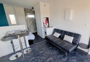 A modern living room with a dark leather sofa, a small round table, and a bar area with stools.