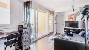 A modern living room with a sofa, a coffee table, and a TV. There is a sliding glass door leading to a balcony.